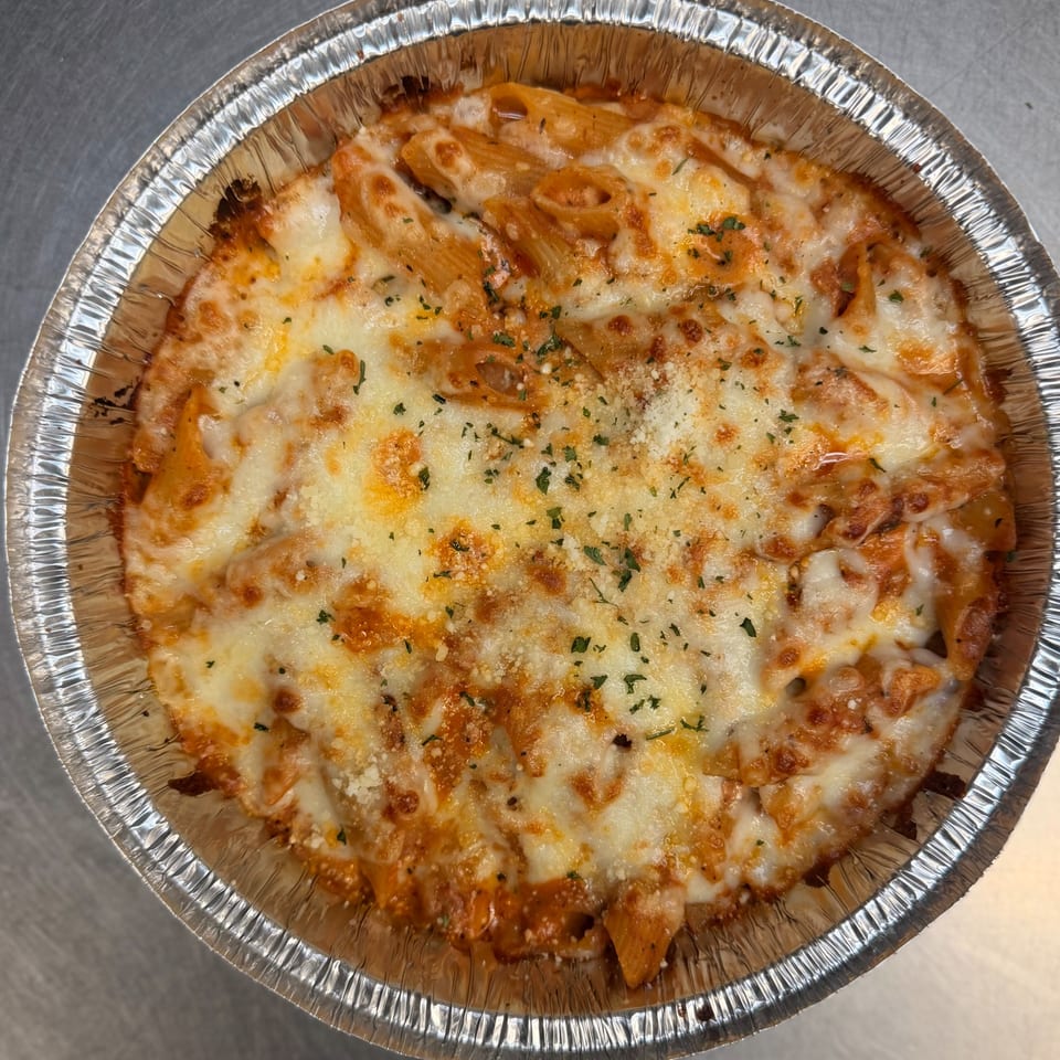 Baked ziti pasta with melted cheese and herbs in a round aluminum foil container.