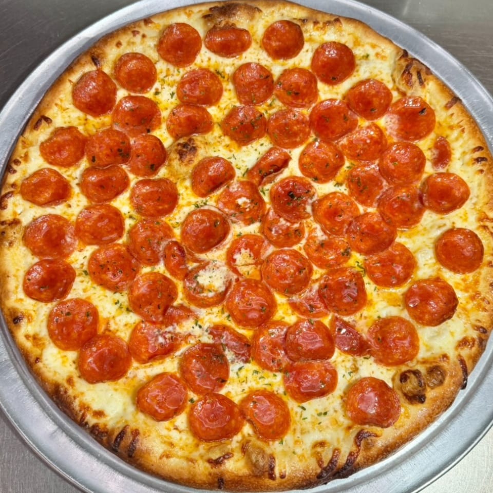 A freshly baked pepperoni pizza, generously topped with cheese and herbs, on a metal tray.