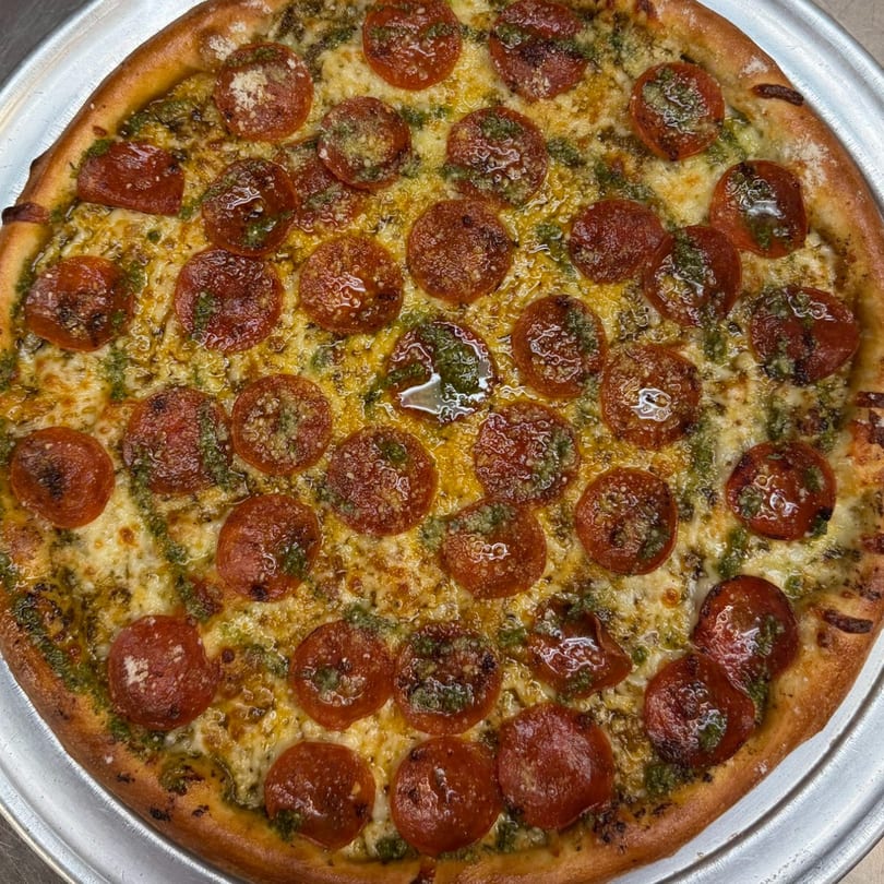 Close-up of a pepperoni and pesto pizza with melted cheese on a metal tray.