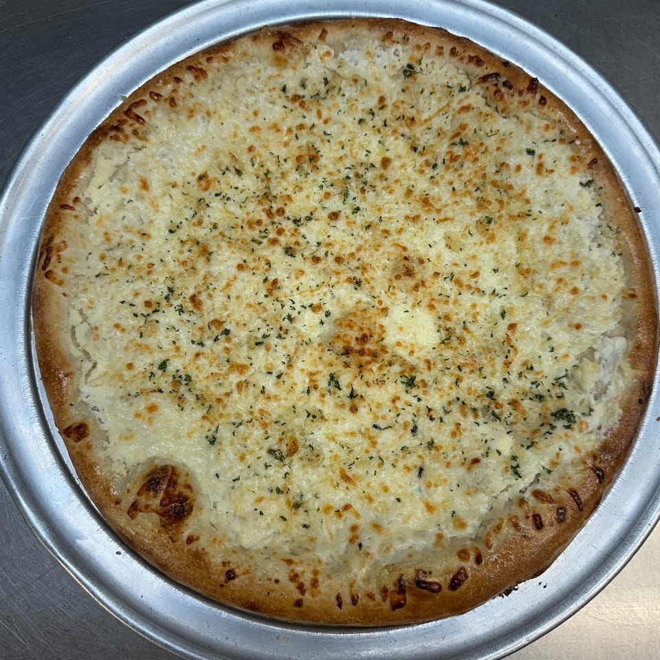 A white pizza with melted cheese and herbs on a metal pizza pan.