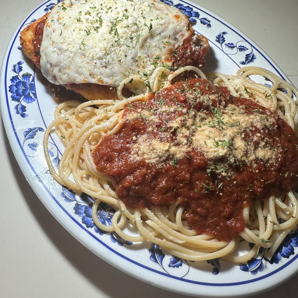Chicken parmesan with melted cheese and herbs, served with spaghetti and red sauce on a blue and white plate.
