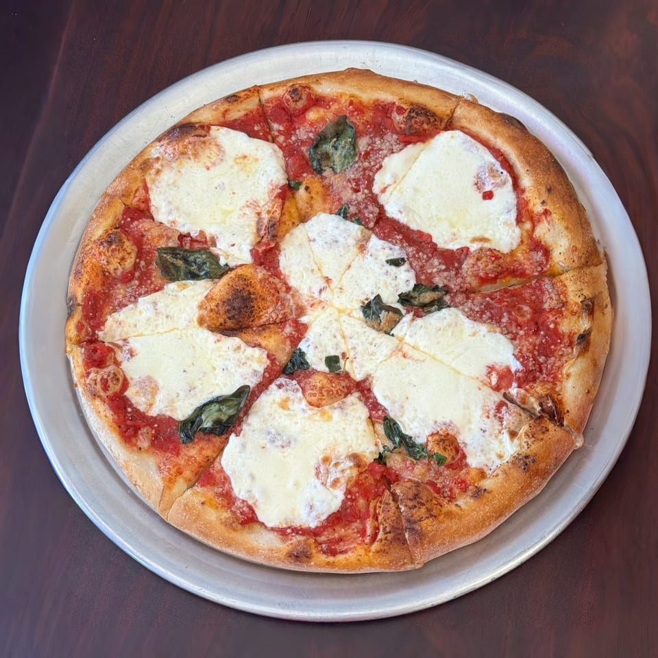 A freshly baked Margherita pizza with melted mozzarella, red sauce, and basil on a metal tray.