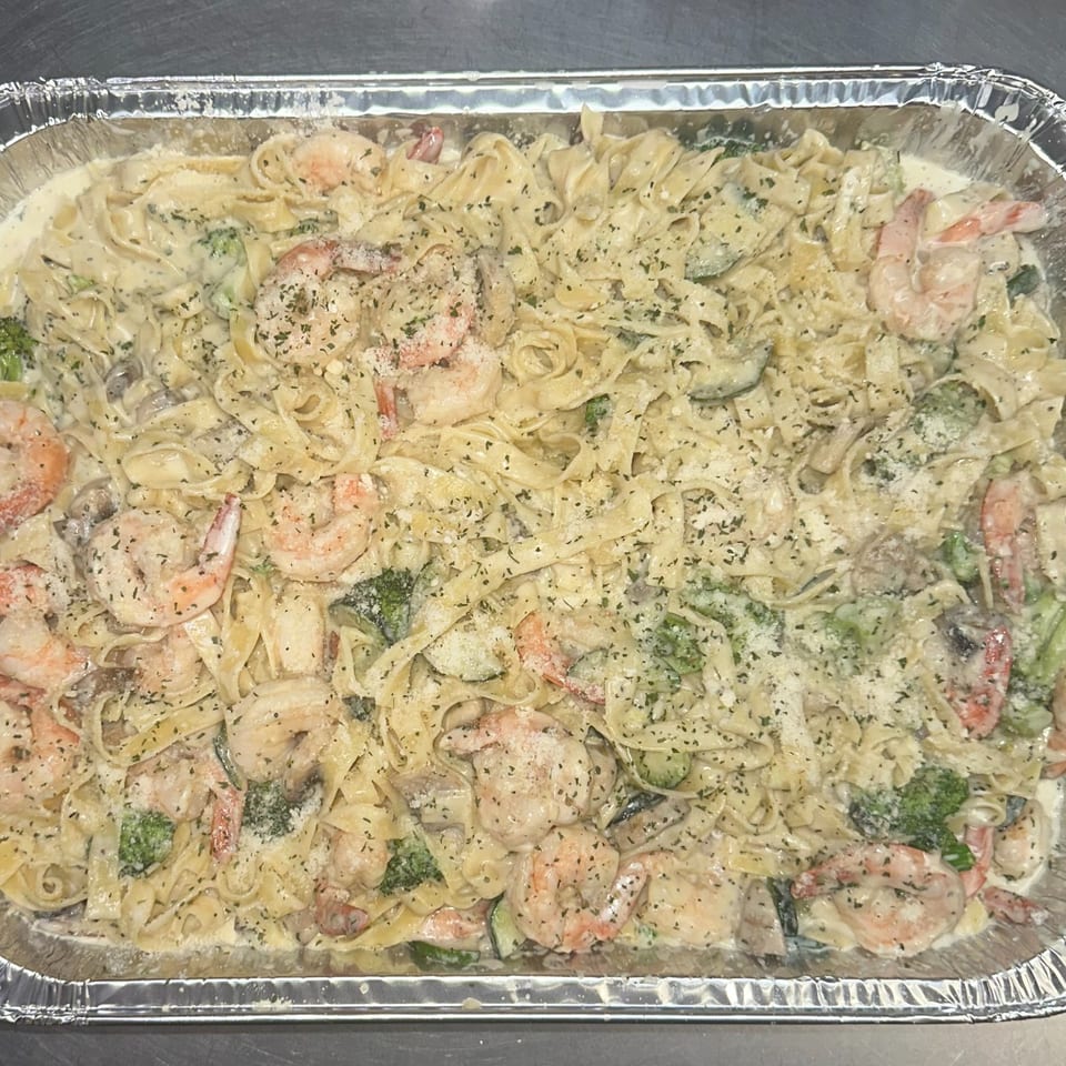 Creamy shrimp fettuccine pasta with broccoli, mushrooms, and zucchini in a foil pan.